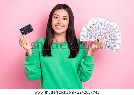 Photo of cute girl cheerful dressed green sweatshirt rising ban card dollars fan isolated pink color background