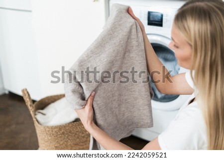 advertising concept of detergent for remove old stain. housewife hold fresh and soft wool sweater after washing in washer machine, checking fabric condition Royalty-Free Stock Photo #2242059521