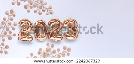 Banner with 2023 inflatable gold balloons and glittering branches on a blue pastel background. New Year's composition with copy space.