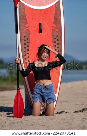 Beautiful traveler girl surfer on holiday portrait with SUP paddle board on the beach on sunny day