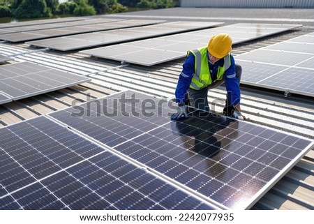 Engineer on rooftop kneeling next to solar panels photo voltaic with tool in hand for installation Royalty-Free Stock Photo #2242077935