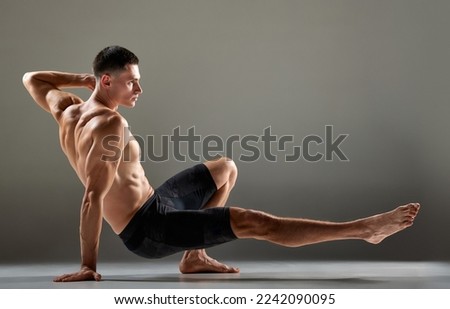Portrait of male flexible muscular athlete showing animal flow sport elements isolated over gray background. Yoga, fitness, trendy sports, beauty of body. Grace and flexibility of human body