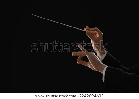 Professional conductor with baton on black background, closeup. Space for text Royalty-Free Stock Photo #2242094693
