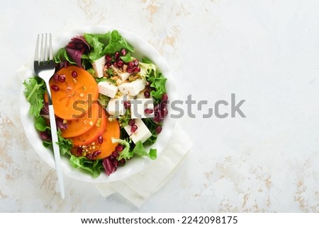 Salad. Fresh green salad with feta cheese, persimmon, pomegranate and pistachio on white plate. Idea for healthy delicious winter Christmas salad. Healthy balanced eating. Top view.