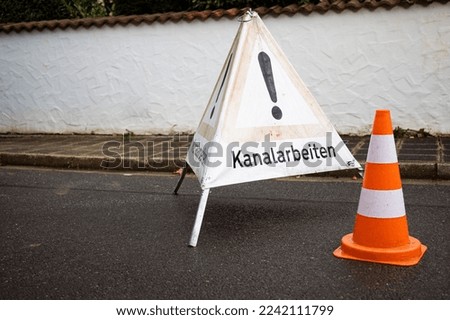 The warning sign and a traffic cone on the street
translation: Sewer works