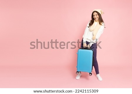 Happy Asian woman traveler holding luggage isolated on pink background, Tourist girl having cheerful holiday trip concept, Full body composition