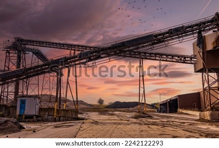 conveyor belts at an abandoned factory at Jutland, Denmark. It is late afternoon and no people are visible in the image. Crows are flying over the site.