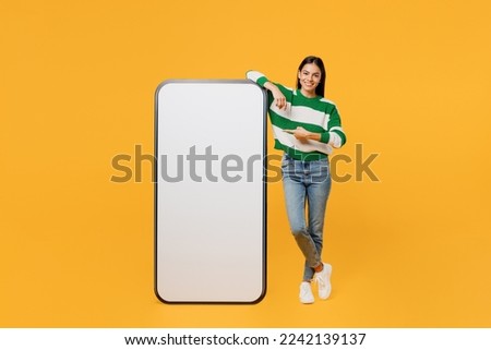 Full body young latin woman wear casual cozy green knitted sweater point index finger big huge blank screen mobile cell phone smartphone with area isolated on plain yellow background studio portrait