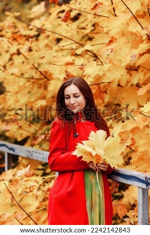 Fall portrait of young woman in red colored coat in autumn season park with leaves, stand deep thinking. Cute model outdoors in Park in golden autumn against background of nature. Copy space