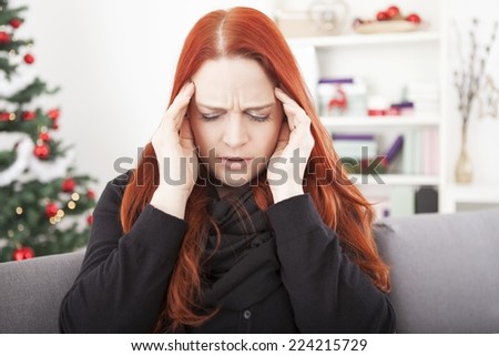 young red haired woman is sick and have headache on christmas