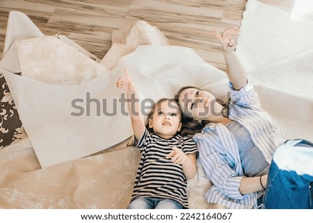 Mom and daughter lie on the floor, on the wallpaper peeled from the wall and plan what kind of room they will have after the repair Reconstruction, repair and design of housing, new interior