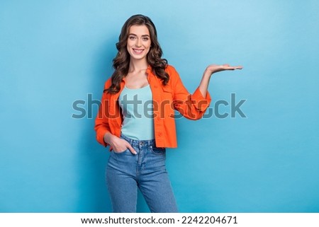 Photo of young positive adorable entrepreneur woman wear stylish casual outfit hold palm empty space new product ad isolated on blue color background