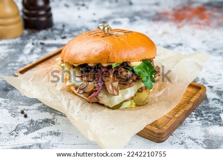 Burger with meat and mushrooms on wooden board on grey table