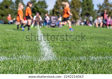 Selective focus on ground level view of soccer field center line with defocused youth girls in background Royalty-Free Stock Photo #2242216063