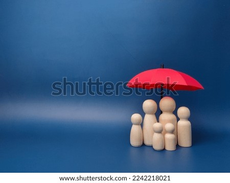 A family of wooden dolls are hiding under a red umbrella, protecting wooden peg dolls, planning, saving families, preventing risks and crises, health care and insurance concepts. Royalty-Free Stock Photo #2242218021