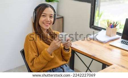 Beautiful woman holding a coffee cup and using a laptop while sitting at her working place in an office.