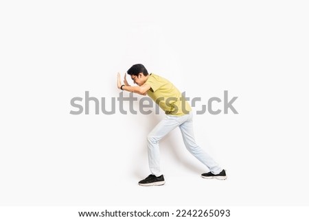 The single skinny young male tries to push something sideways. The full body of an Asian or Indonesian person. Isolated photo studio with white background. Royalty-Free Stock Photo #2242265093