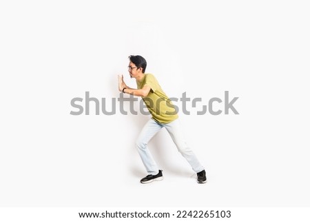 The single skinny young male tries to push something sideways. The full body of an Asian or Indonesian person. Isolated photo studio with white background. Royalty-Free Stock Photo #2242265103