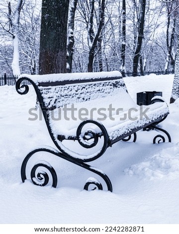 A bench in the park covered with snow in winter. Winter weather and first snow concept. Royalty-Free Stock Photo #2242282871