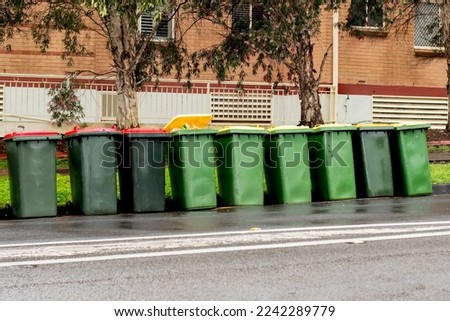 Australian garbage wheelie bins with yellow and red lids lined up on the street near residential building for council rubbish collection. Royalty-Free Stock Photo #2242289779