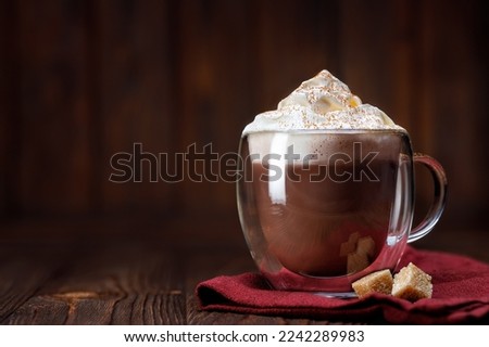cocoa or hot chocolate with whipped cream topping in glass cup on wooden table