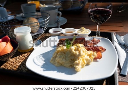 Breakfast set. Pan of fried eggs with bacon, sage and bread on dark serving board over black background