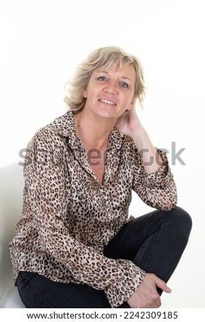 senior blond sixties woman with blonde mature hair posing sitting in studio with hand on chin arm knee