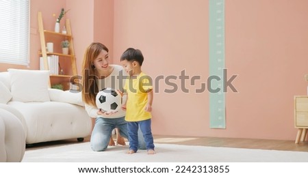 asian happy mother and her child son are playing with soccer ball together in living room at home