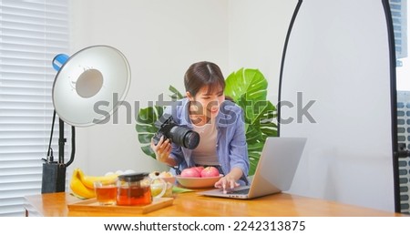 Female Asian photographer taking picture of healthy food checking image with laptop