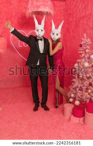 The couple in poligonal rabbit masks closeup on the pink background are celebrating New 2023 year. Celebration party