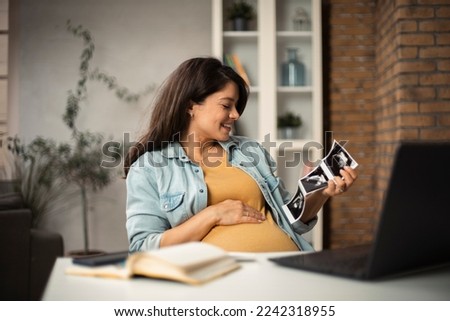 Beautiful young pregnant woman holding ultrasound pictures of her baby. Businesswoman having video call