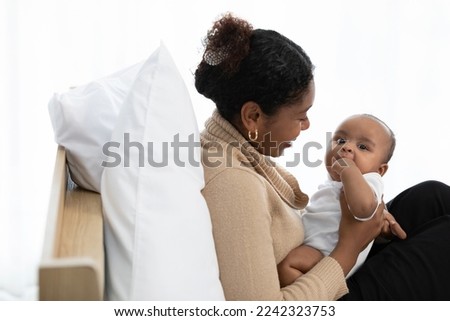 African young mother carrying and kissing with her adorable baby on bed