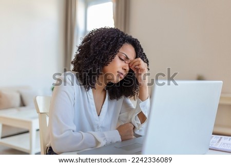 Exhausted businesswoman having a headache in home office. African American creative woman working at office desk feeling tired. Stressed business woman feeling eye pain while overworking Royalty-Free Stock Photo #2242336089
