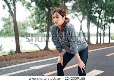 Tired young asian woman resting after running hard in the road at the park after a daily exercise, running jogging for his fitness in the warm summer morning. Royalty-Free Stock Photo #2242339155