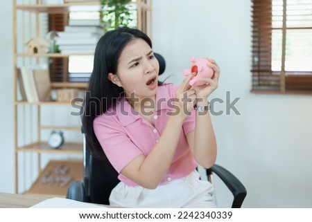 Portrait of an Asian female businesswoman showing a serious and anxious expression in an SME business , but no money in the pink pig piggy bank , saving plans.