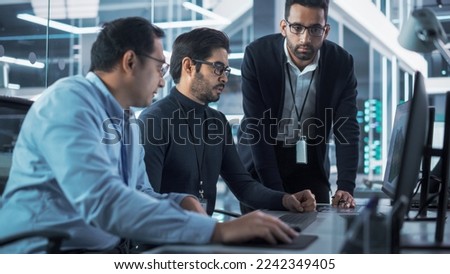 Team of Three Handsome Talented Young Engineers Use Computer to Discuss a Technological Project in Industry 4.0 Modern Factory Office. Group of Scientists Work in Research and Development Center. Royalty-Free Stock Photo #2242349405