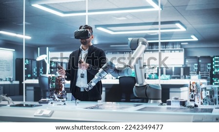 Robotics Engineer Operating a Futuristic Robotic Arm, Using a Virtual Reality Headset and Controllers to Perform Tasks. Work in Research and Development High Tech Facility Startup. Royalty-Free Stock Photo #2242349477