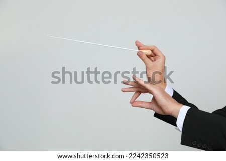 Professional conductor with baton on light grey background, closeup. Space for text Royalty-Free Stock Photo #2242350523