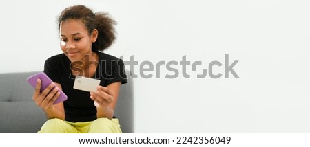 Photo of smiling American African woman holding smart phone and credit card in hand. Panoramic image with empty copy space