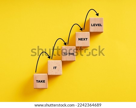 Business career path for growth and success concept. Wooden block ladder with the message take it to the next level with stepping up arrows. Royalty-Free Stock Photo #2242364689
