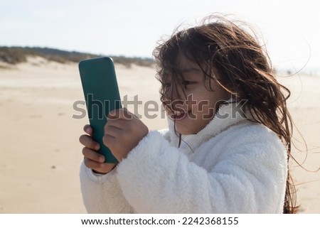 Little Japanese girl with mobile phone on beach. Dark-haired child holding device and looking at screen. Childhood, technology concept