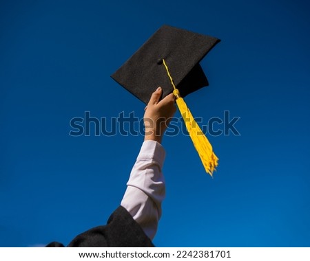 Close-up of a woman's hand with a graduation cap against the blue sky.  Royalty-Free Stock Photo #2242381701