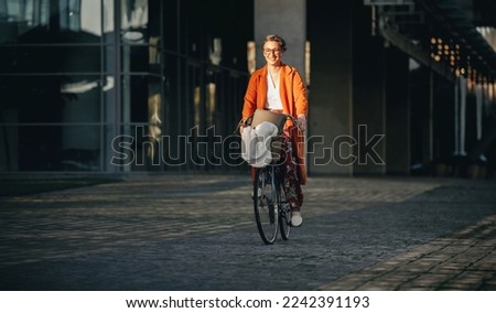 Happy business woman smiling cheerfully while riding a bicycle to work in the city. Mature business woman enjoying her eco friendly morning commute to the office.