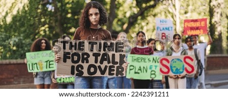 Young girl looking at the camera while leading a march against climate change. Group of multicultural youth activists protesting against global warming. Teenagers joining the global climate strike.