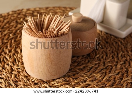 Wooden holder with many toothpicks on wicker mat, closeup Royalty-Free Stock Photo #2242396741