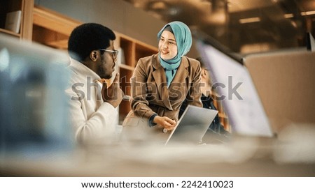 Two Coworkers Collaborating and Celebrating Their Accomplishment in a Modern Office. Muslim Female Trainer Using Laptop to Onboard a Black Male Customer Support Agent and Answering His Question. Royalty-Free Stock Photo #2242410023