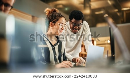 Portrait of Two Creative Colleagues Using Laptop to Discuss Work Project at Office. Young Black Technical Support Specialist Helping Female Customer Relationship Coordinator. Teamwork Concept Royalty-Free Stock Photo #2242410033