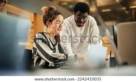 Portrait of Two Creative Colleagues Using Laptop to Discuss Work Project at Office. Young Black Technical Support Specialist Helping Female Customer Relationship Coordinator. Teamwork Concept Royalty-Free Stock Photo #2242410035