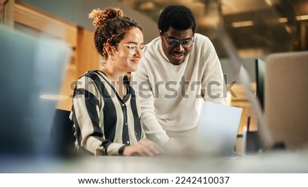 Portrait of Two Creative Colleagues Using Laptop to Discuss Work Project at Office. Young Black Technical Support Specialist Helping Female Customer Relationship Coordinator. Teamwork Concept Royalty-Free Stock Photo #2242410037