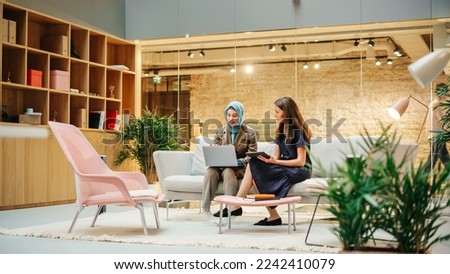 Two Creative Colleagues Collaborating Over a Work Project Using Computer and Tablet at Office. Female E-commerce Marketing Manager Discussing with Muslim Female Media Planner. Medium